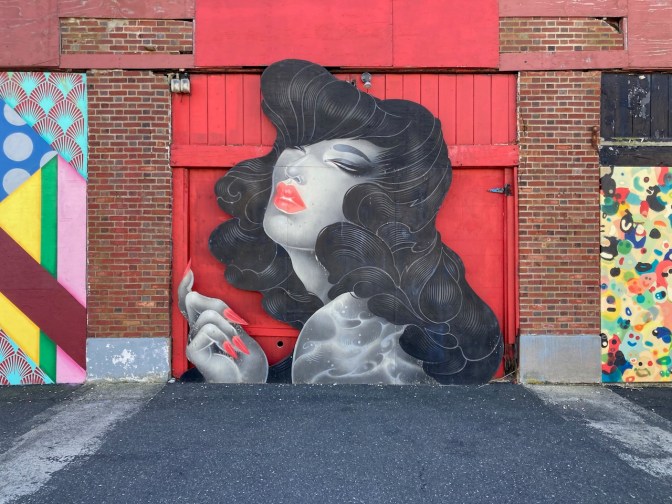 Mural of woman painted on red doors of brick building.