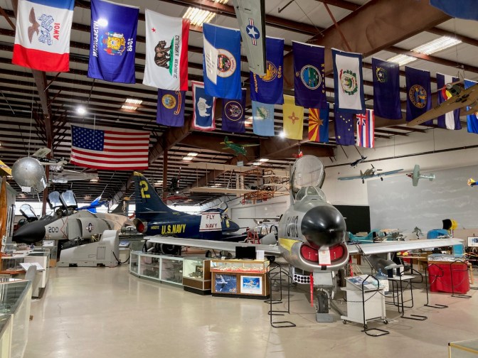 Museum with aircraft and displays in former hangar. Flags hang from ceiling.