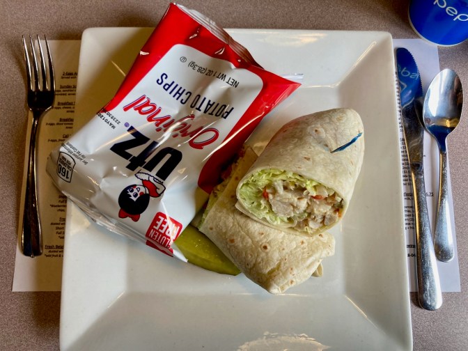 Chicken wrap on white plate with bag of chips.
