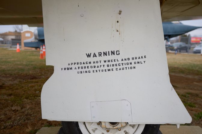 Sign on flap beneath Phantom jet that reads WARNING APPROACH HOT WHEEL AND BRAKE FROM A FORE OR AFT DIRECTION ONLY USING EXTREME CAUTION.