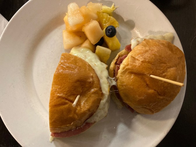 Egg, pork roll, and cheese sandwich on white plate, with side of fruit.