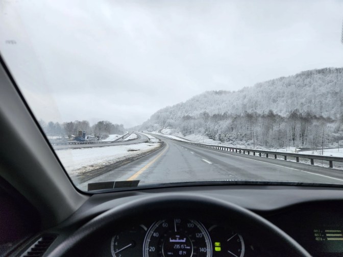 View of highway, with trees covered in snow, from behind dashboard of 2014 Honda Accord.