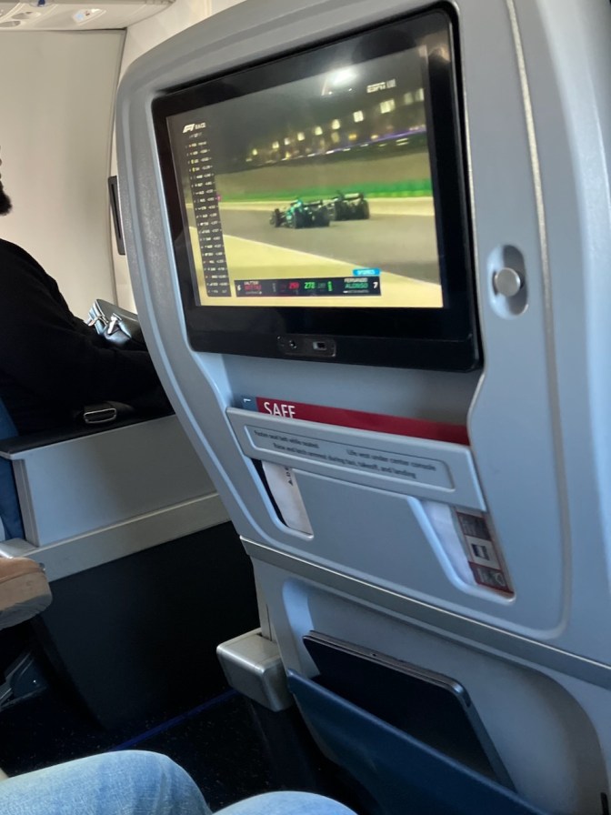 TV monitor on airplane seat with Formula One race.