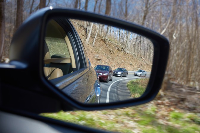 Lineup of cars heading up mountain road, captured in rear view mirror.