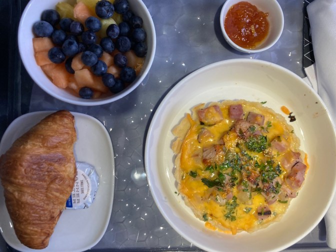 Meal tray with croissant, quiche, fruit.