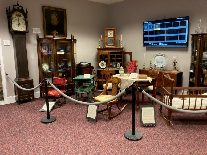 Exhibits in museum containing artifacts of Bolling family life, including a grandfather clock, a rocking chair, tables, dressers, cabinets, and a cradle.