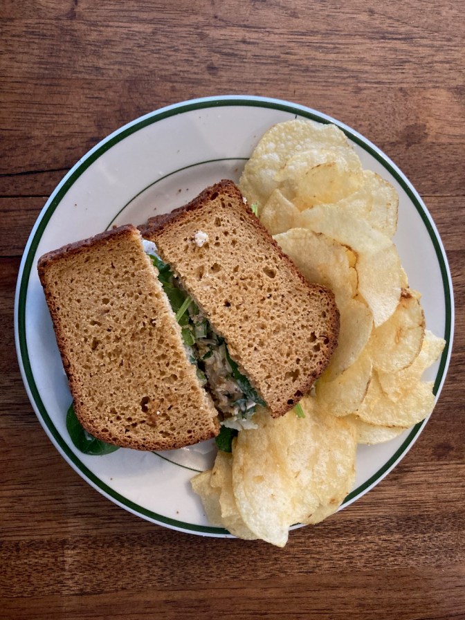 Chicken salad sandwich and potato chips, on white plate.