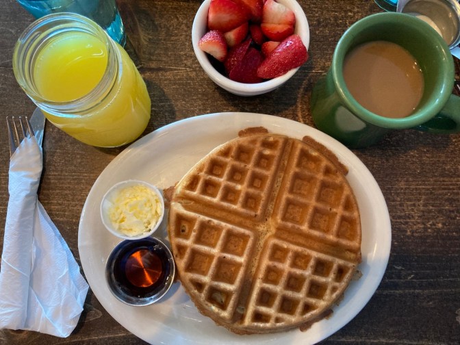 Waffle on plate, with glass of orange juice cup of fruit, and mug of coffee.