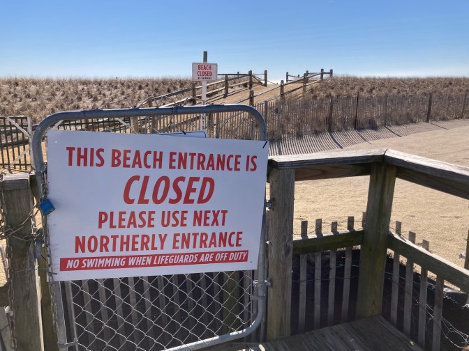 Closed gate in front of dunes, with sign that reads THIS BEACH ENTRANCE IS CLOSED PLEASE USE NEXT NORTHERLY ENTRANCE.