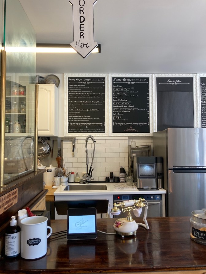 Counter inside cafe, with chalkboard menu on wall in background.
