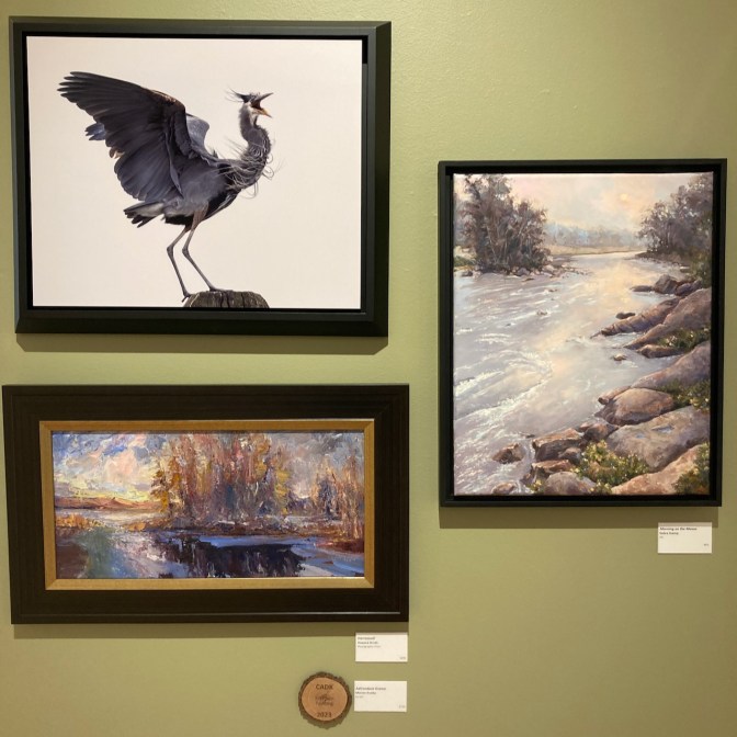 A photo of a heron, along with two paintings of landscapes, on wall.