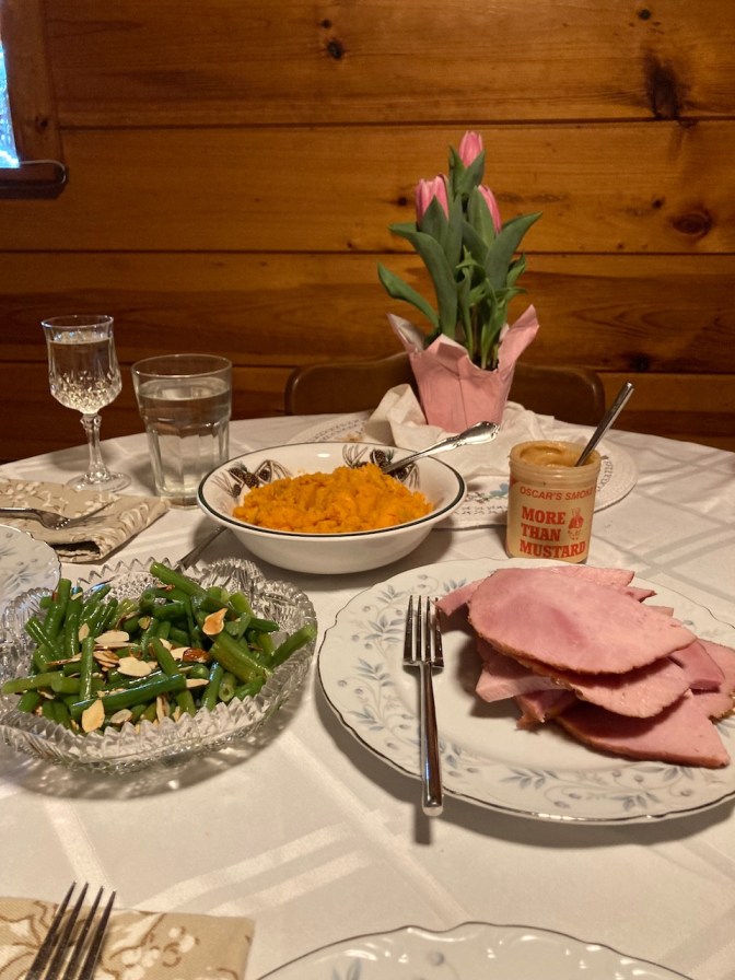 Dining room table with plate of ham, dish of green beans, and bowl filled with sweet potatoes.