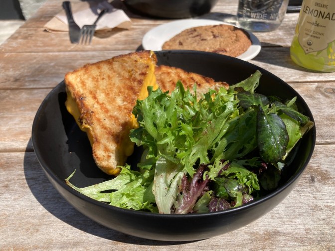 Grilled cheese and salad in a black bowl.