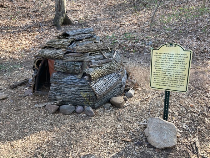Sall wigwam on display, with a sign post near it.
