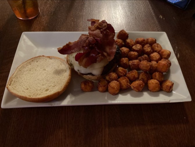 Cheeseburger and tater tots on white plate.