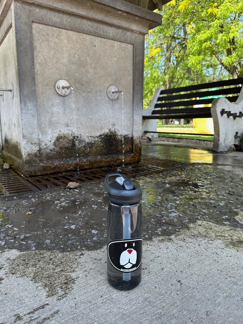 Water bottle on ground beside spring water faucet.