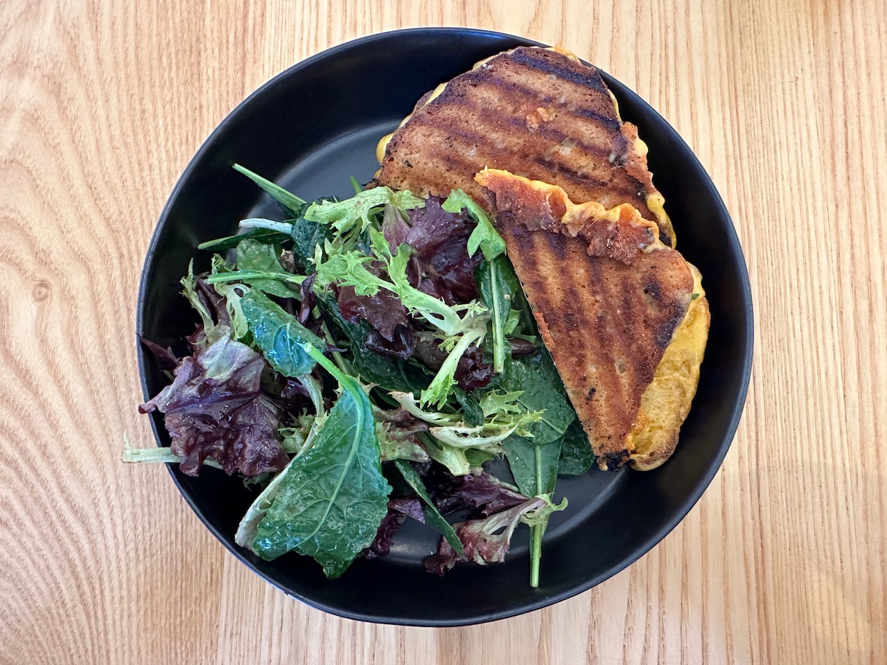 Black bowl with grilled cheese sandwich and a salad.