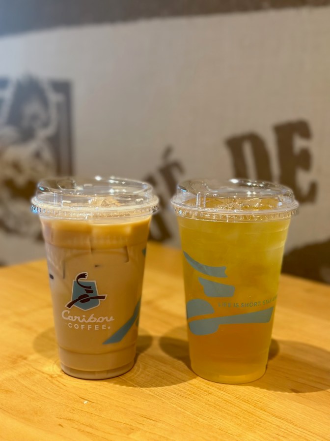 Latte and ice tea in two plastic cups on table.