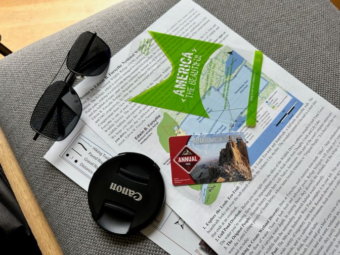 Chair with map of park, National Park Service Annual Pass, sunglasses, and lens cap.