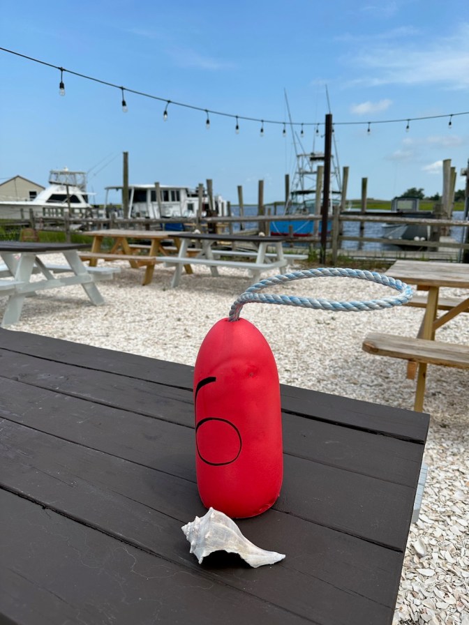 Buoy on picnic table, with other picnic tables in background, and shapes tied up at dockside in far background.