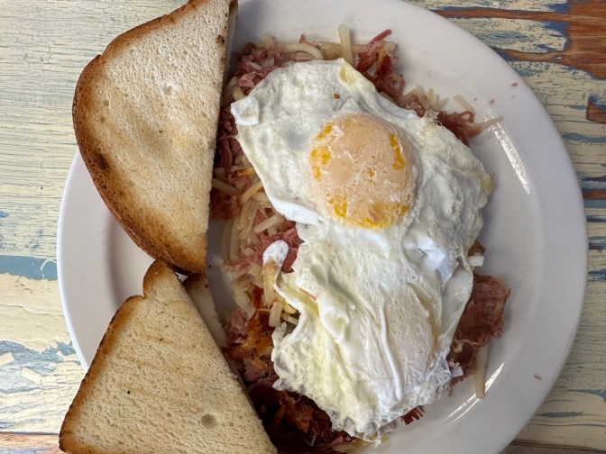 Eggs over easy over corned beef hash, with gluten-free toast, on white plate.