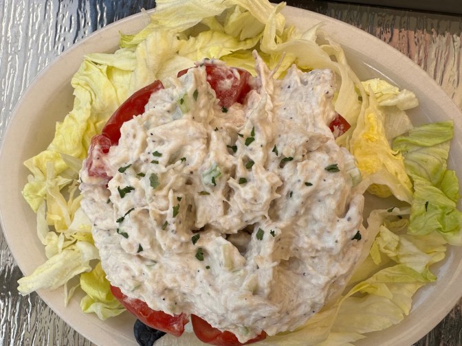 Stuffed tomato on bed of lettuce on white plate.