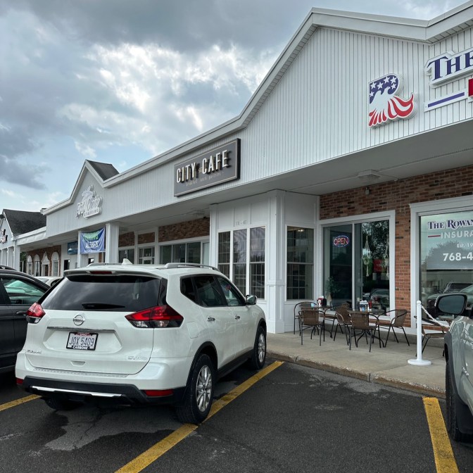 Exterior of strip mall with sign for City Cafe hanging above door.