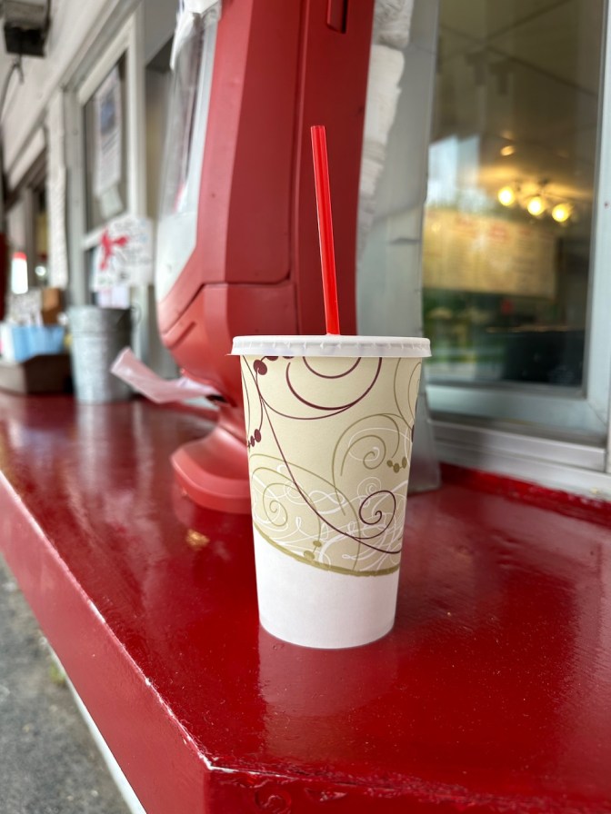 Milkeshake cup on red counter outside restaurant.