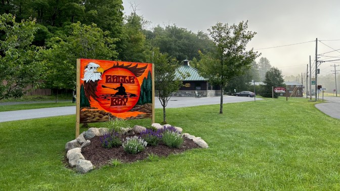 Sign outside of Eagle Bay Welcome Center that says Eagle Bay, and has mural of kayaker paddling at sunset.