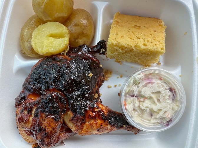 Barbecue chicken, cornbread, coleslaw, and potatoes in styrofoam container.