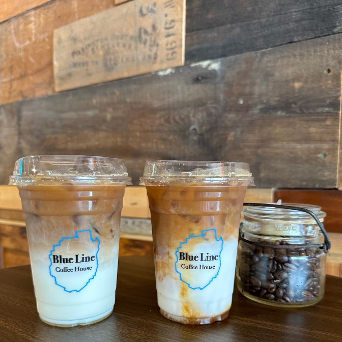 Two lattes in plastic cups on wooden table.
