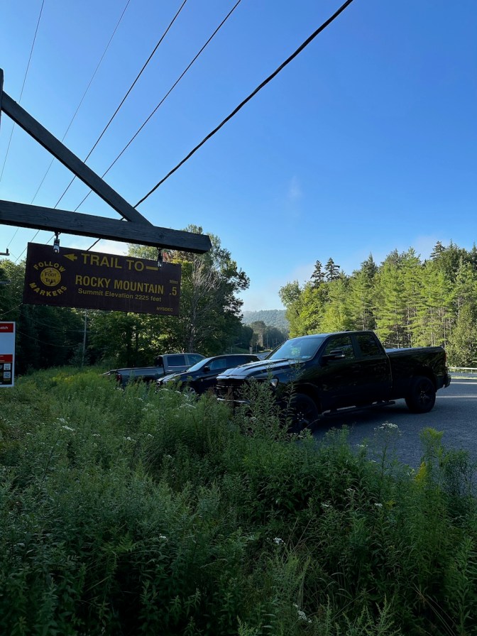 View of trailhead sign for Rocky Mountain, with cars in parking lot behind it.