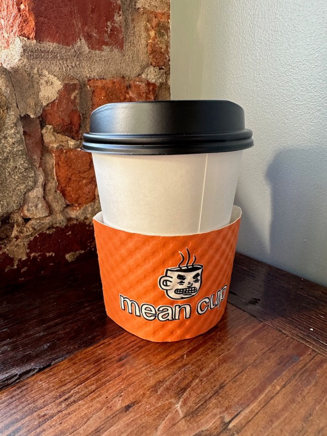 Paper coffee cup with Mean Cup sleeve.