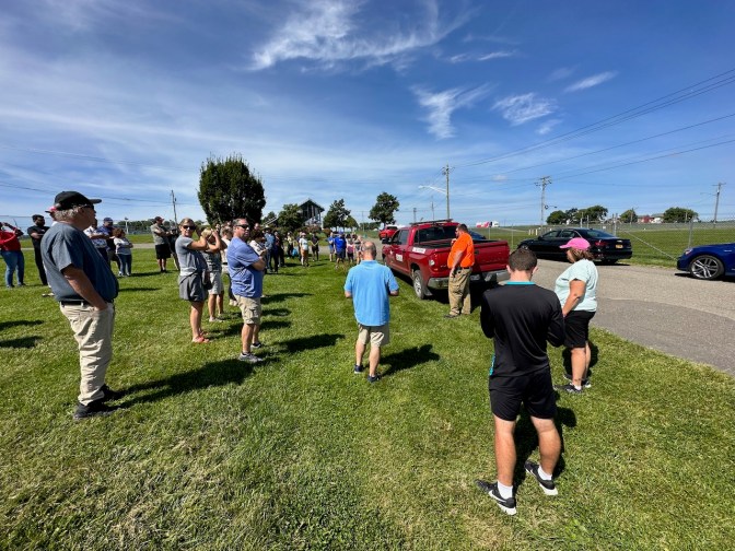 Drivers gathered around safety marshal on grass field.