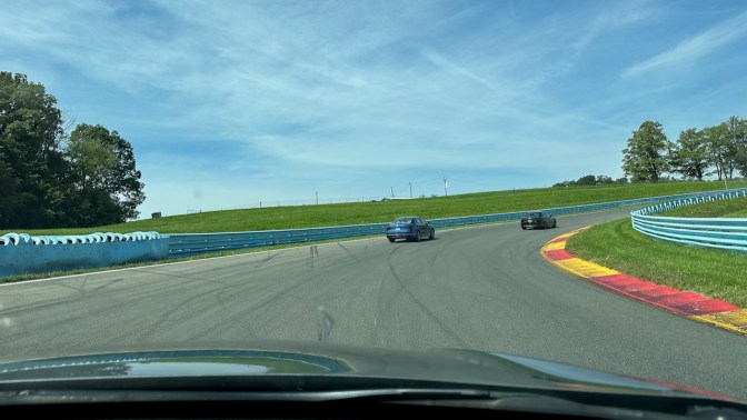 Two cars ahead on race track, viewed from behind dashboard of 2012 Honda Accord.
