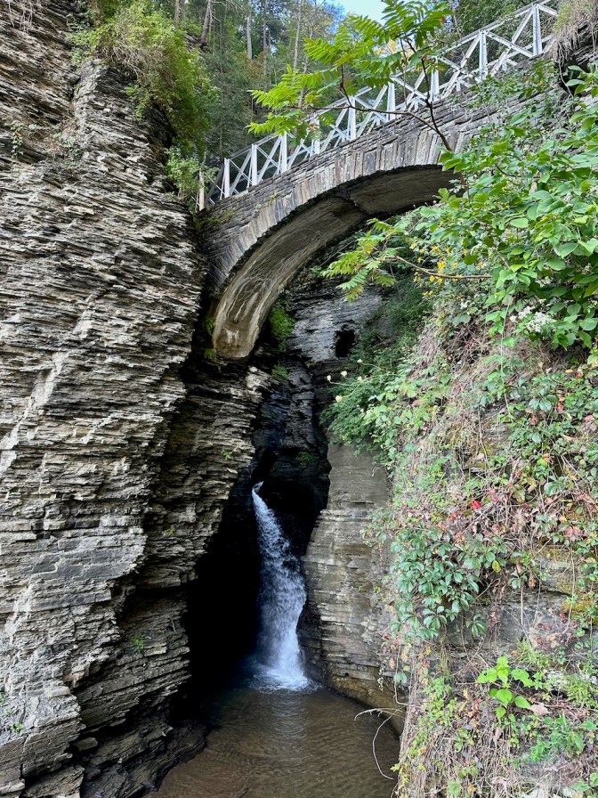 Stone bridge over gorge, with waterfall in background.