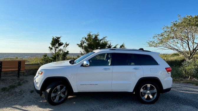 2014 Jeep Grand Cherokee parked in front of dunes by sea.