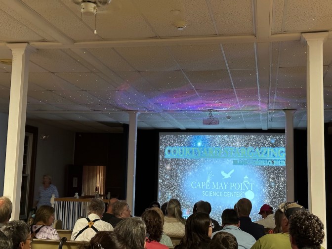 Slideshow projected onto screen, with audience of people in chairs in front of screen.