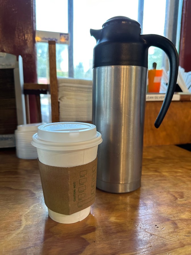 Coffee cup beside cream pitcher on counter.
