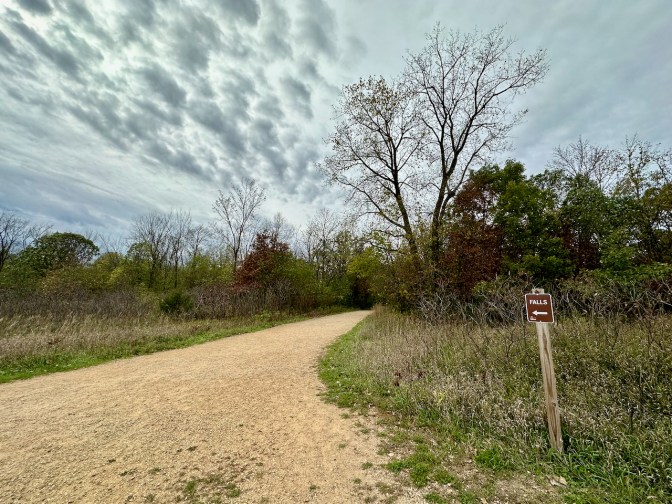 Dirt path through park, with signs that reads FALLS and an arrow pointing down path.