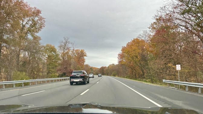 Tree-lined I-287 under gray skies. The leaves on the trees are changing colors for autumn.