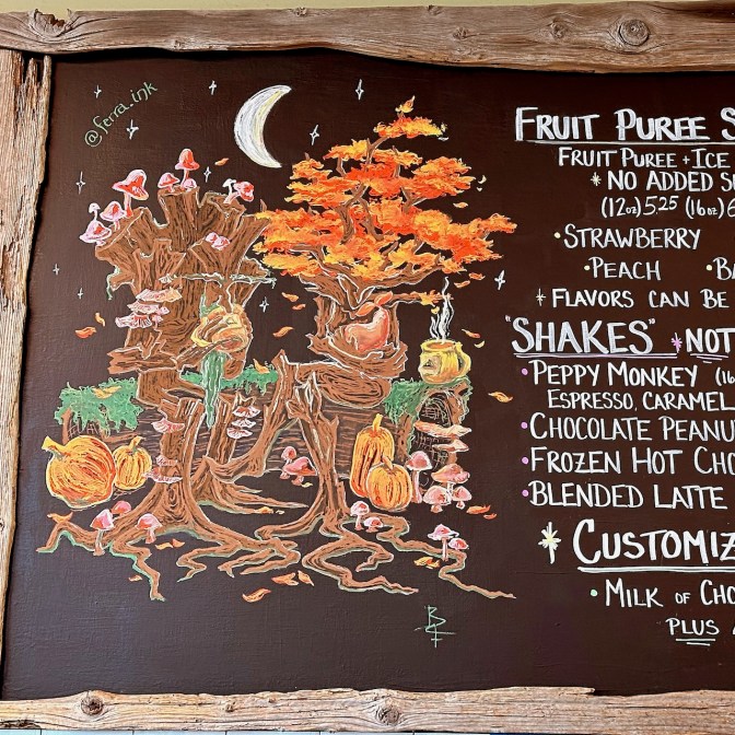 Chalkboard with items for order in coffee shop and chalk drawing of autumn scene.
