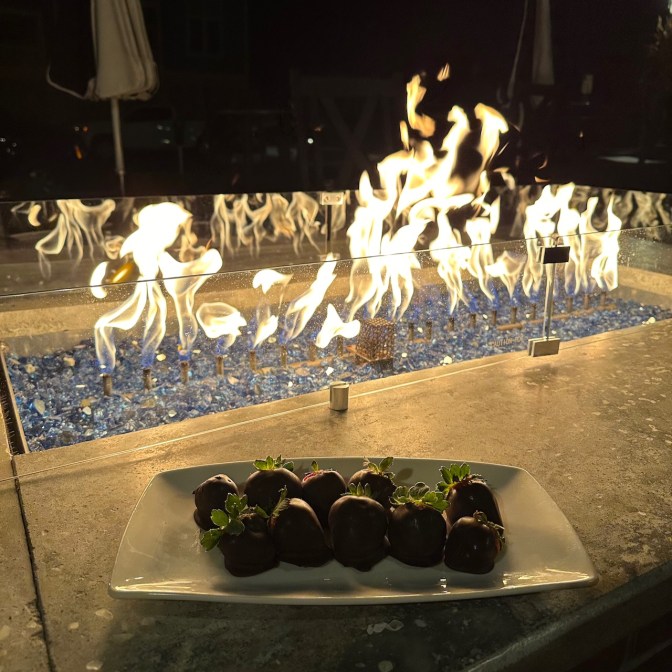Fire table on patio, with plate of chocolate covered strawberries on table.