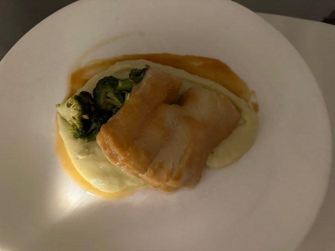 Fish, potatoes, and broccoli on white plate.