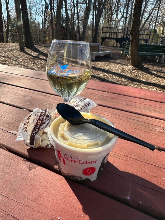 Cup of clam chowder and glass of wine on wooden table.