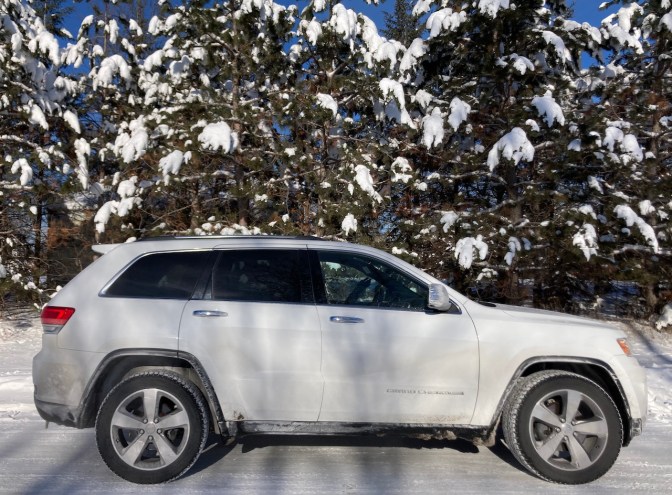 2014 Jeep Grand Cherokee, parked in front of snow-covered pine trees.