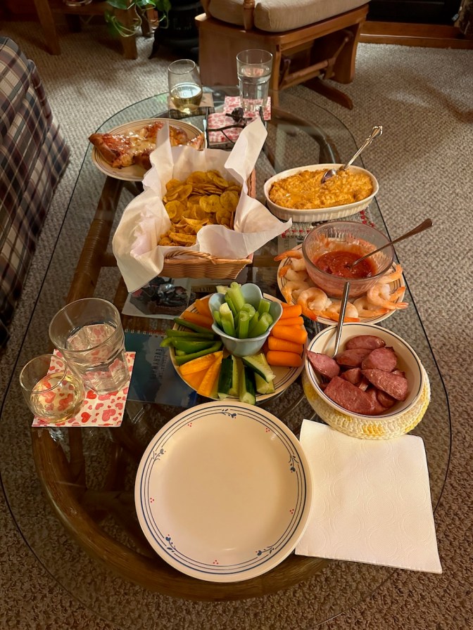 Spread of food on glass table including vegetables, kielbasa, shrimp cocktail, buffalo chicken dip, and chips.