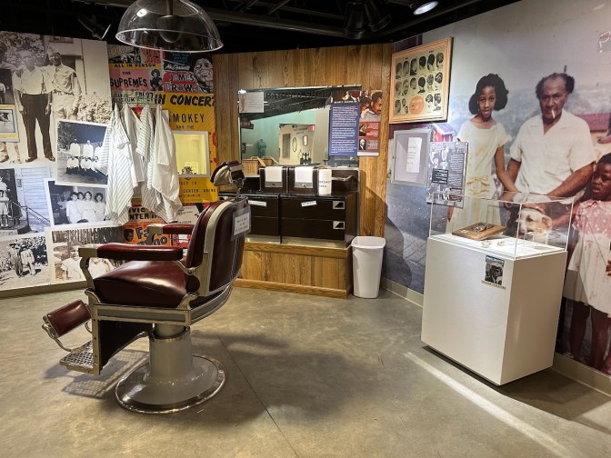 Display of items from African American barbershop, including a barber's chair in middle of display.