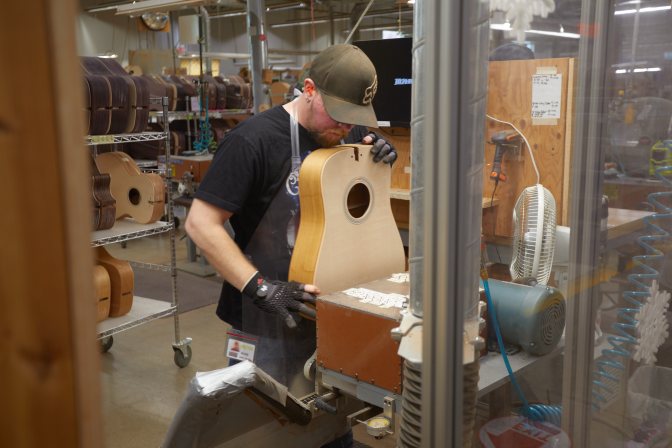 Man sanding guitar body in factory.