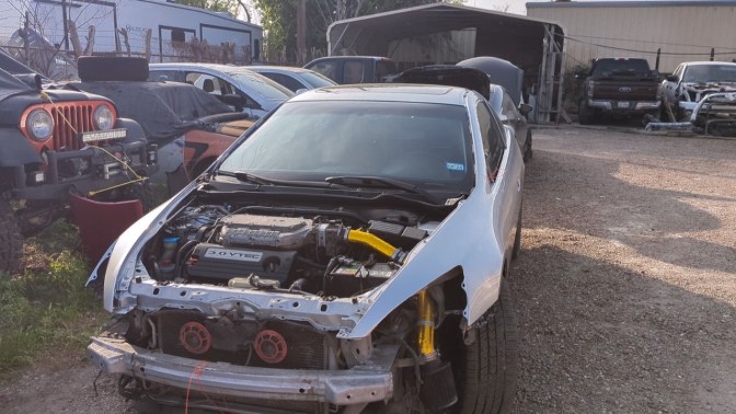 2003 Honda Accord coupe parked in paint shop lot. It is missing front bumper and hood.
